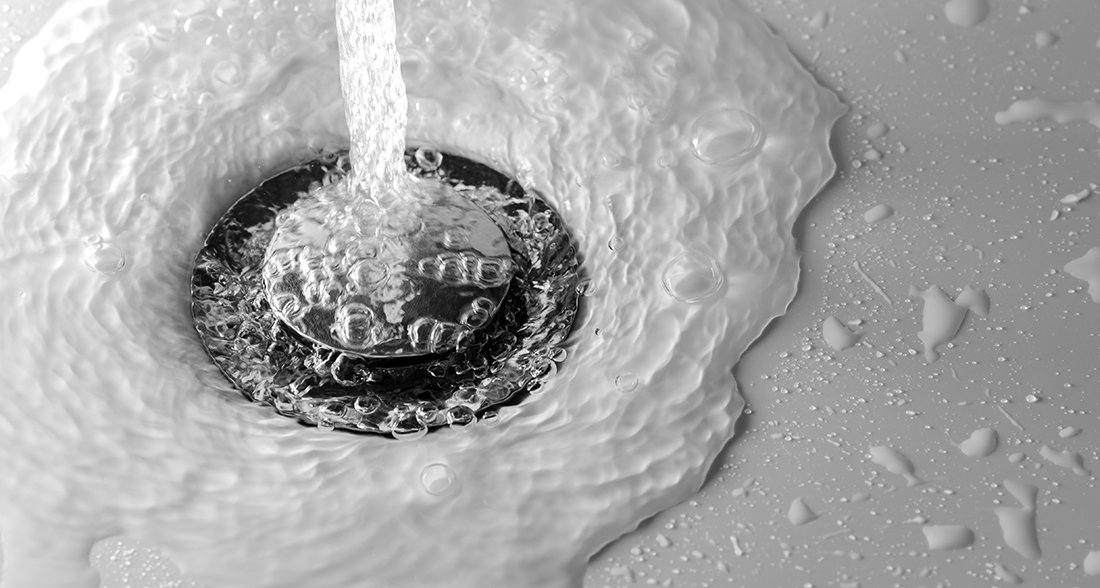 Water Drains Into The Hole Of White Sink In The Bathroom